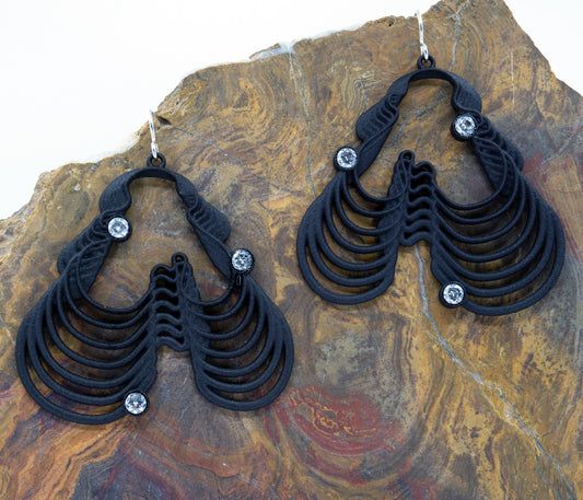 A pair of black, wave-shaped earrings with clear cubic zirconia accents, displayed against a textured background.