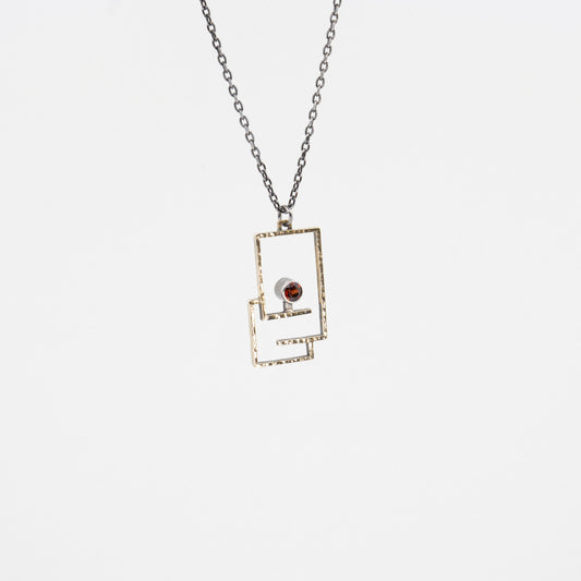 A CAD designed and cast in brass pendant with a red garnet stone in a simple modern design, attached to a sterling silver neck chain.