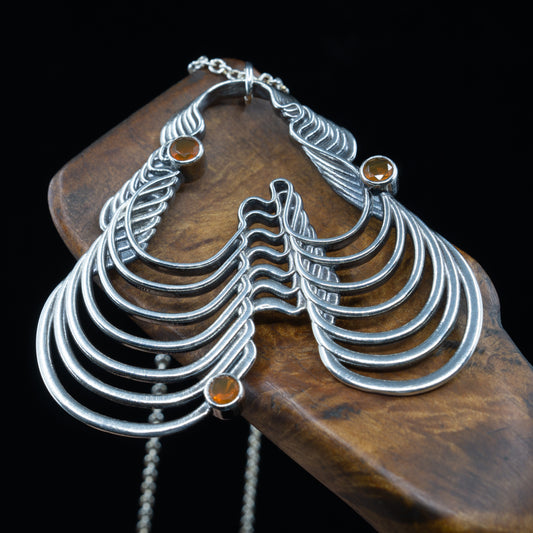 A silver pendant with a geometric wave pattern design, with 3 3mm fire opals, displayed on a wooden necklace holder.