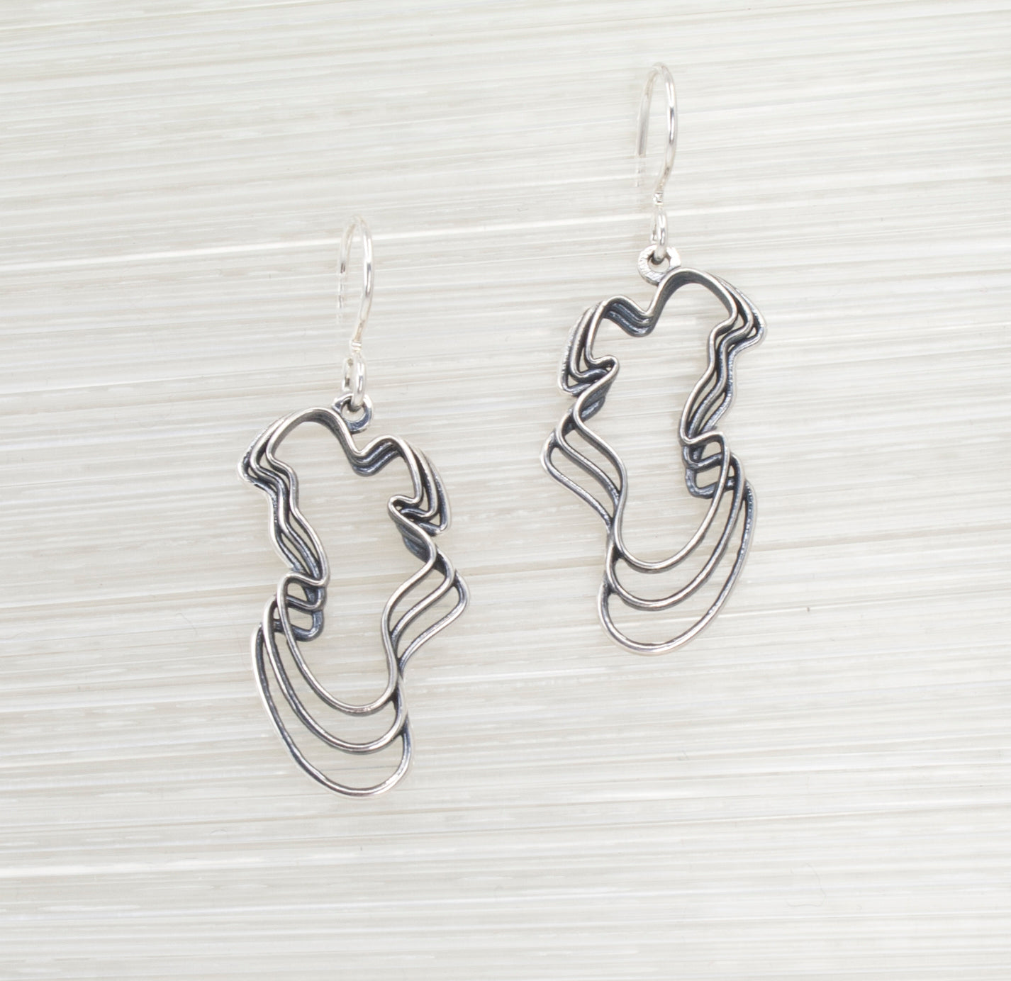 Sterling Water Waves Curvy Earrings on a Textured White Background